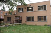 Two-story brick nursing home building with windows, entrance stairs, and a green lawn in front.