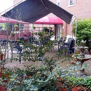 Outdoor patio with metal tables and chairs under a canopy near a brick building.