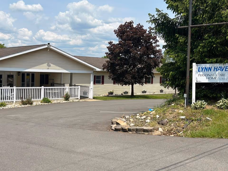 A single-story beige facility with a white porch railing and a sign reading Lynn Haven Personal Care Home beside a parking area.