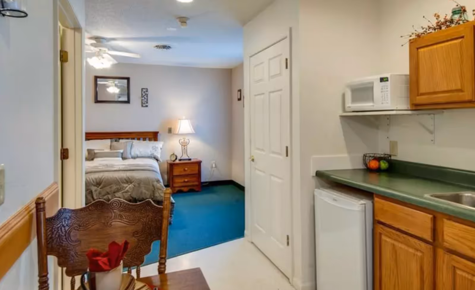 Studio-style room showing a kitchenette with microwave and sink on the right and a bed with nightstand in the background.