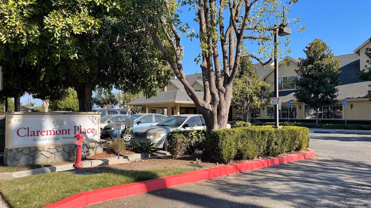 Front entrance and driveway of Claremont Place assisted living with the facility sign, parked cars, trees, and the building facade.