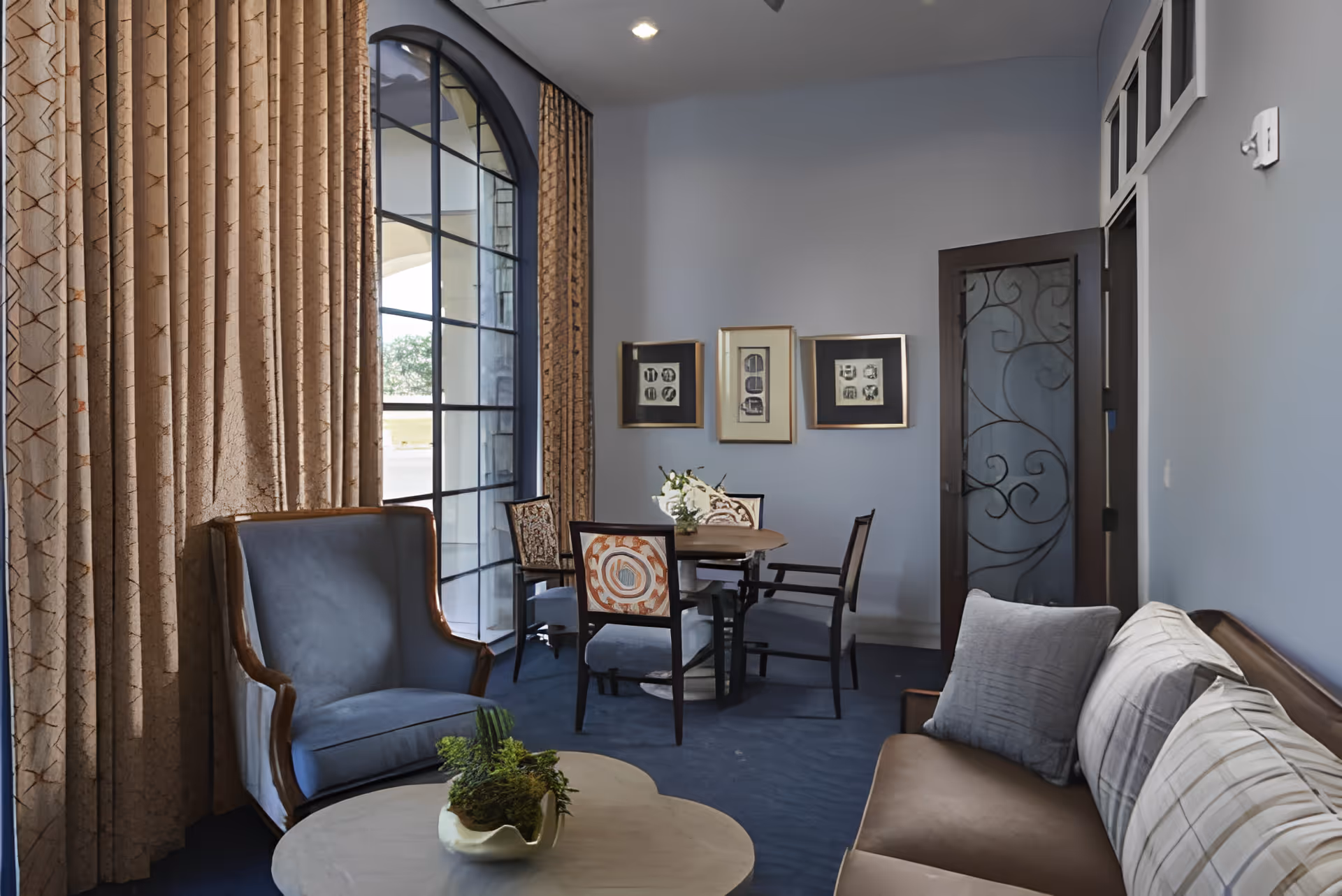 A comfortable lounge with armchairs, a sofa, coffee table, and a small dining table near a large arched window.