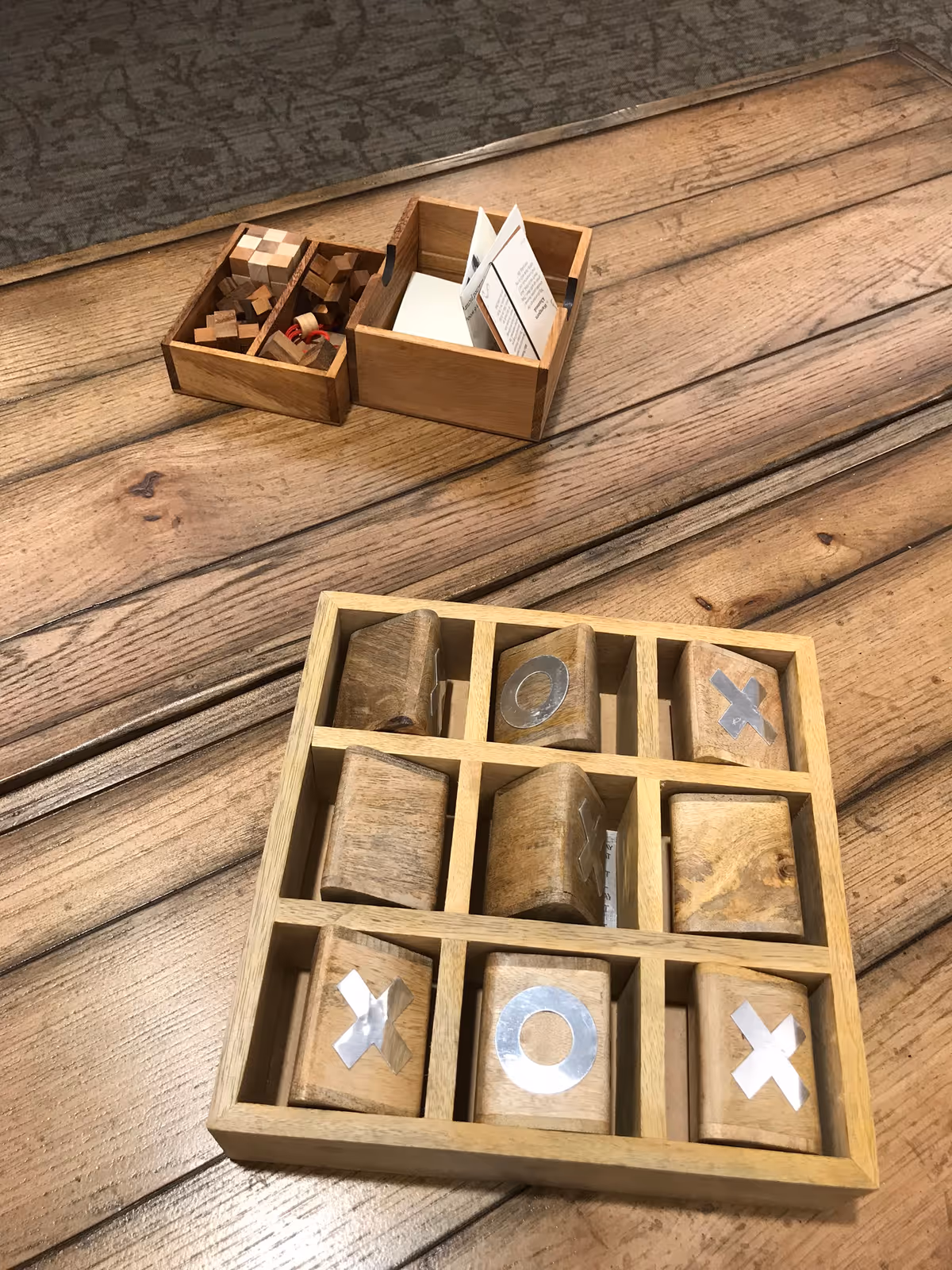 A wooden tic-tac-toe set and small wooden puzzle boxes arranged on a rustic wooden table.