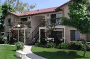 Two-story stucco senior living building with red-tiled roof, balconies, and landscaped front lawn.