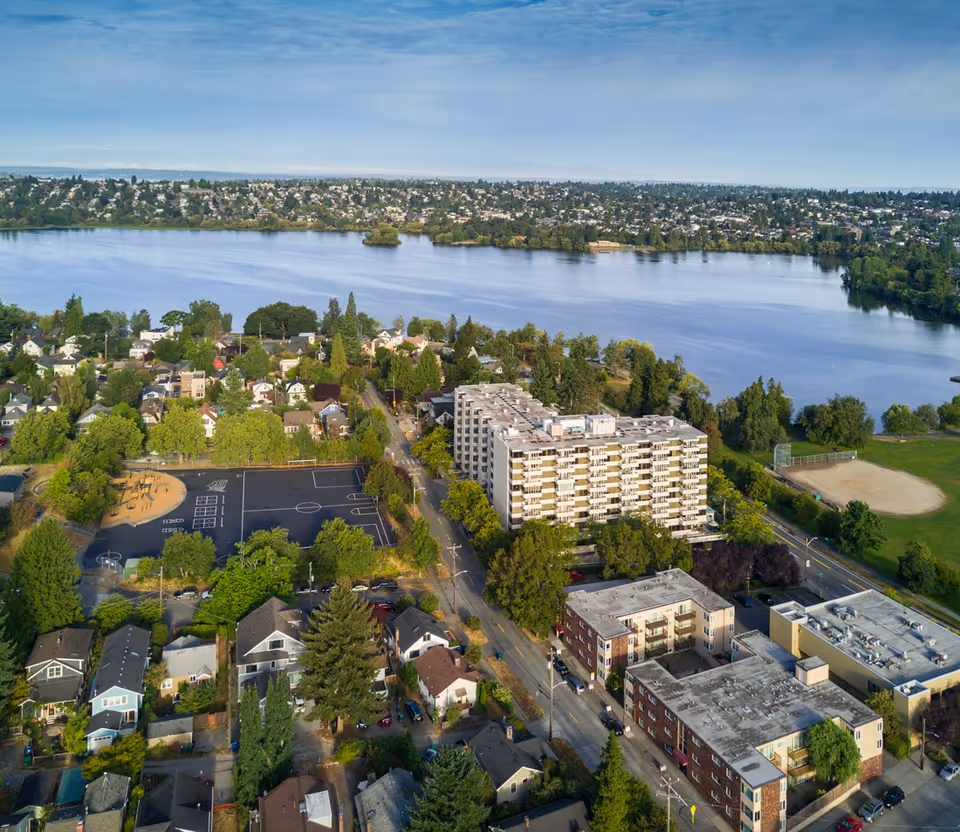 Aerial view of a lakeside neighborhood showing a mid-rise residential/senior living building near a large lake, surrounded by houses, streets, and parks.
