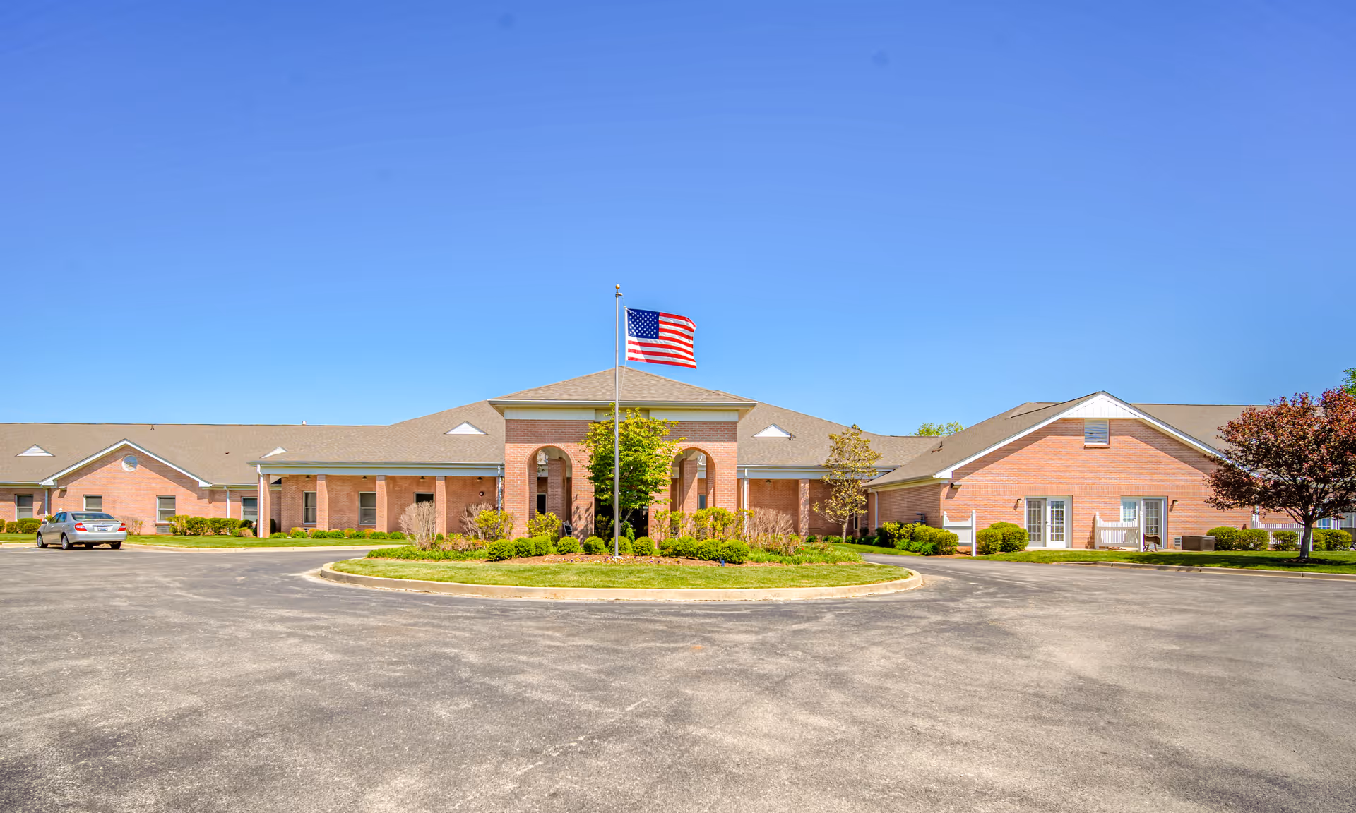 Front exterior of a brick senior living facility with an American flag and circular driveway.