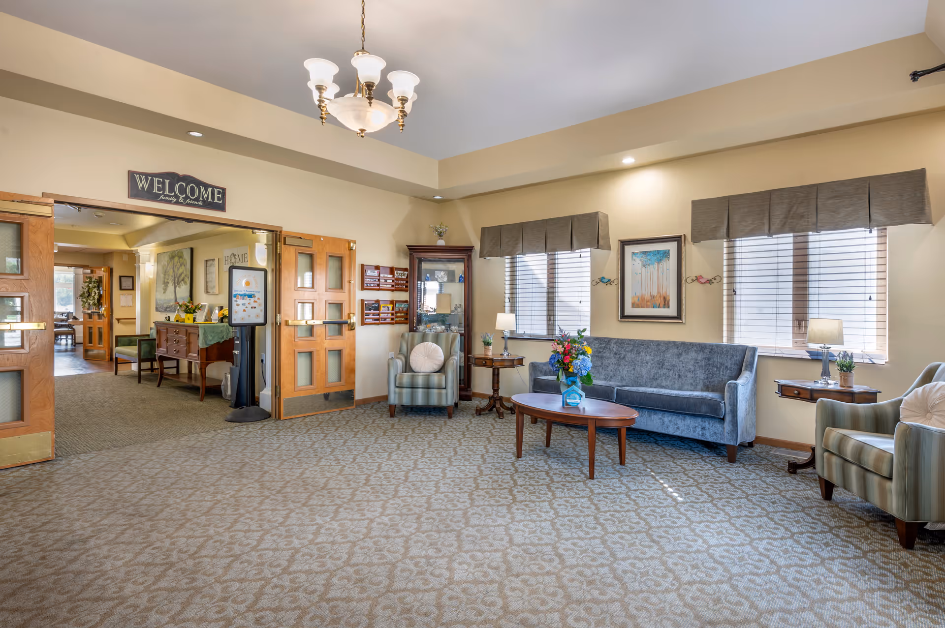 Well-lit reception lounge with sofas, armchairs, a coffee table and a 'WELCOME' sign over double doors.