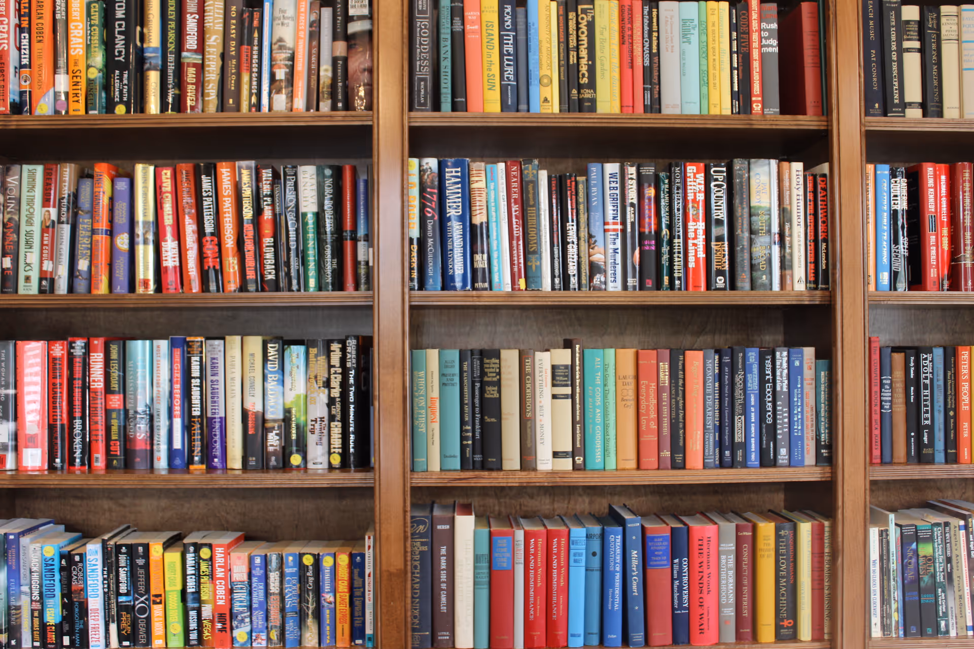 A wooden bookshelf filled with a variety of books arranged vertically on multiple shelves. The books have colorful spines with different titles and authors visible.