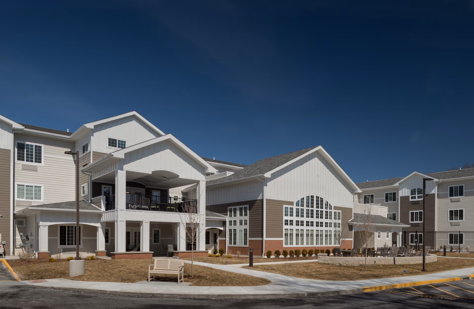 Front exterior of a multi-story senior living building with large windows, a covered entrance, and a small landscaped courtyard.