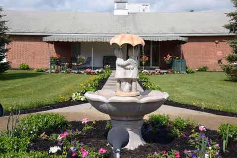 Front view of a brick senior living facility with a fountain and colorful garden.