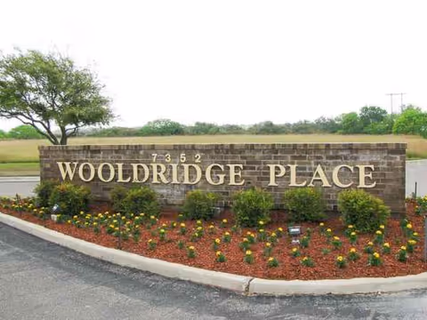 Brick entrance sign Wooldridge Place with shrubs and a mulched flower bed.