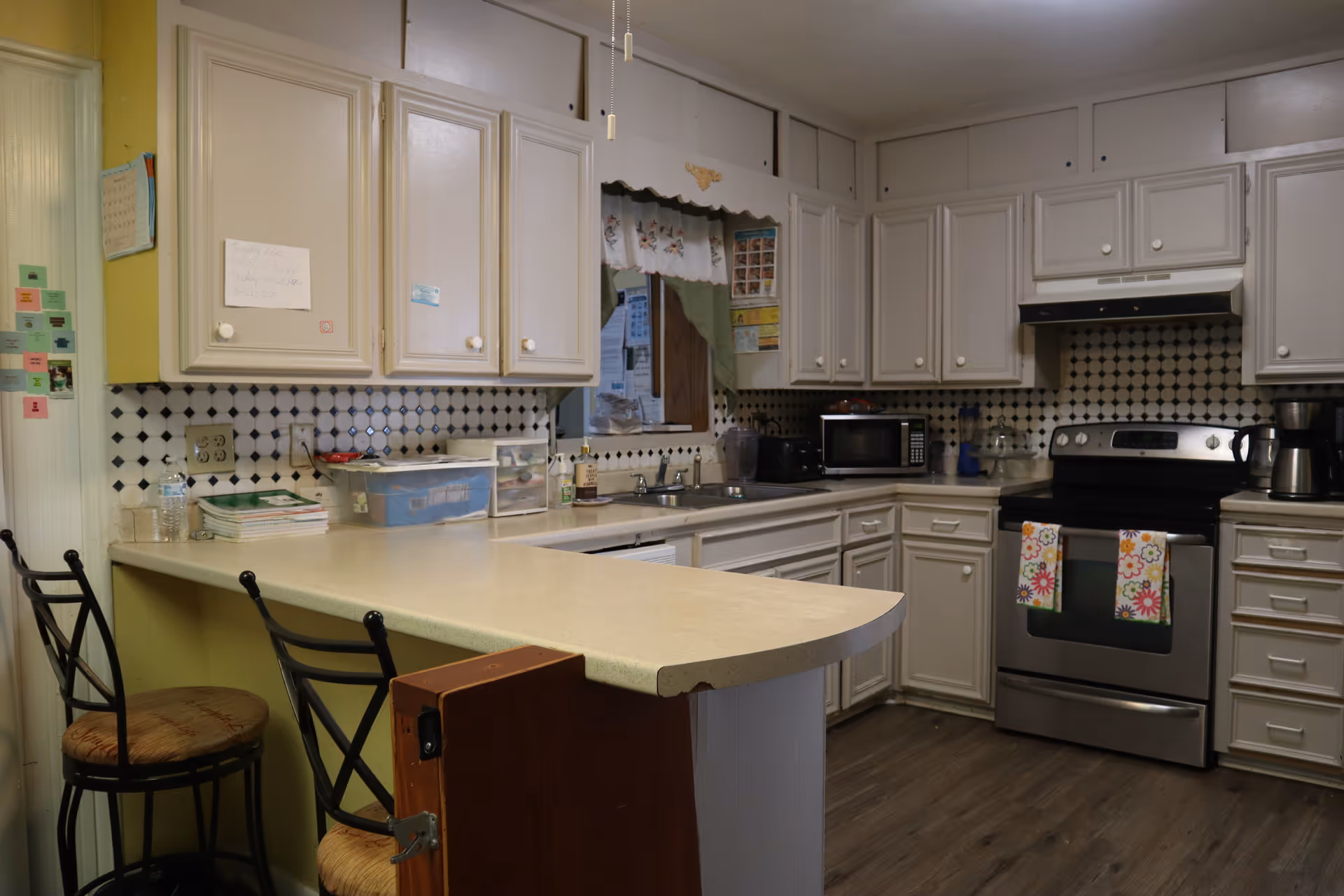 A home kitchen with white cabinets, a countertop peninsula with two bar stools, and stainless steel stove and appliances.