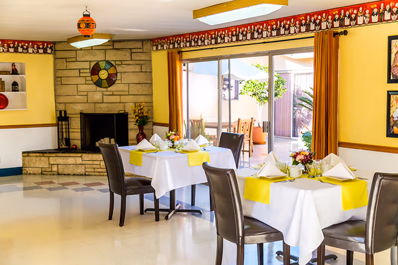 Bright dining room with tables set for a meal, leather chairs, a fireplace and sliding glass doors to an outdoor patio.
