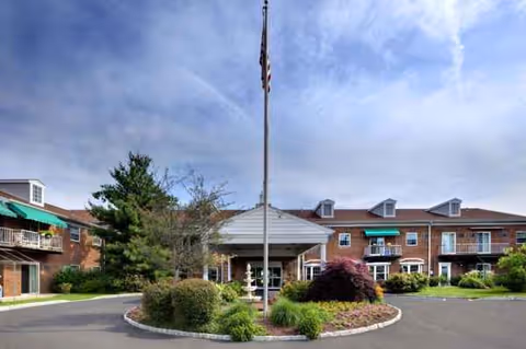 Exterior view of Gwynedd Estates building with entrance, flagpole, and landscaped circular driveway.
