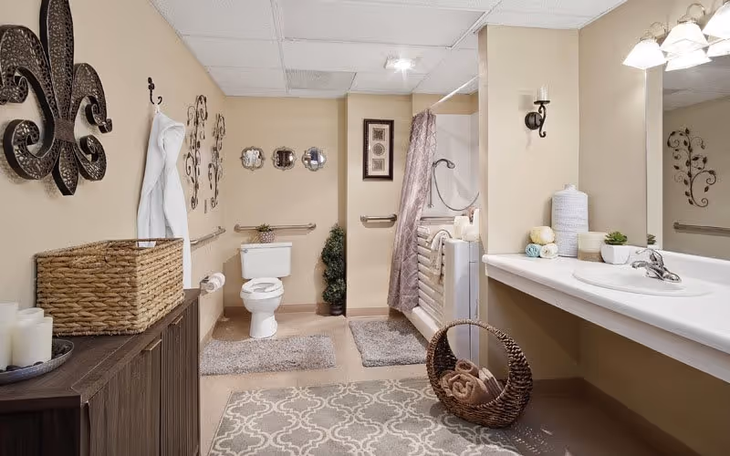 Accessible beige bathroom with a toilet, sink and mirror, walk-in bathtub with shower curtain, and decorative wicker baskets.
