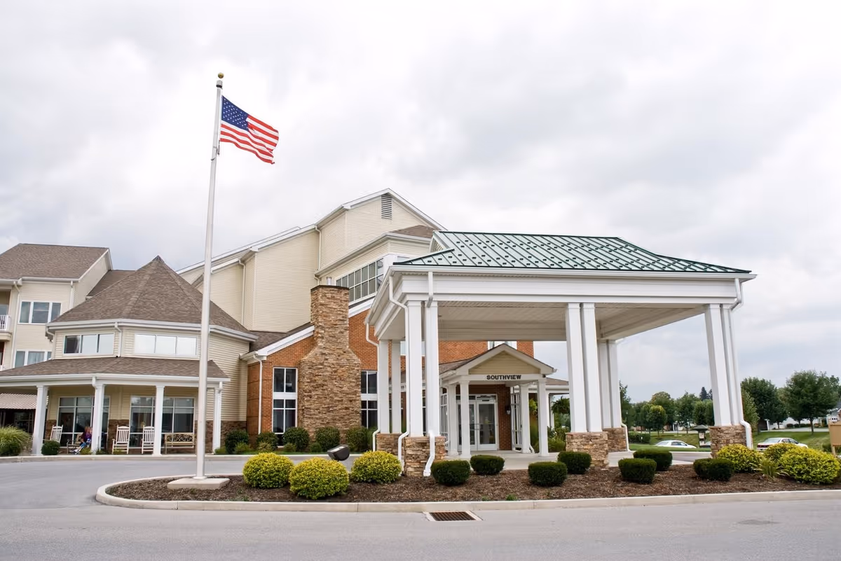 Front entrance of Homewood Living Martinsburg with a covered porte-cochere, American flag on a pole, and landscaped driveway.