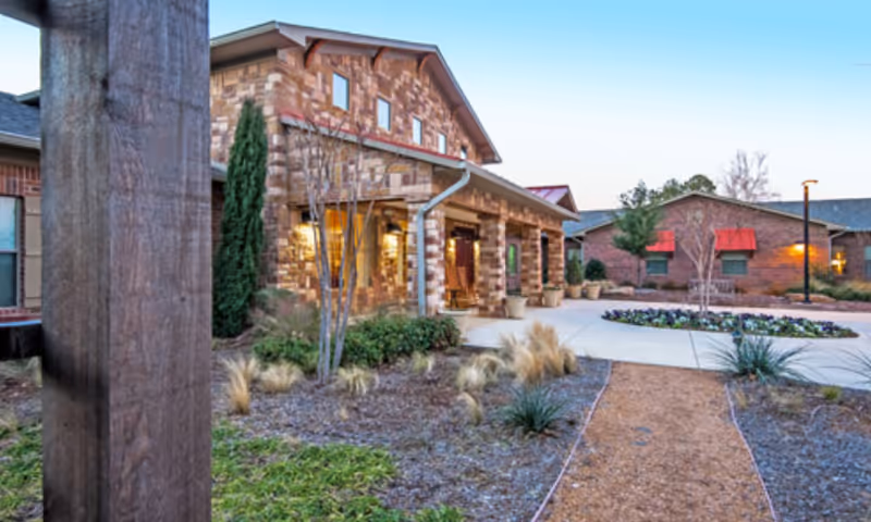 Front exterior of a stone-faced assisted living building with a covered entrance, walkway, and landscaped grounds.