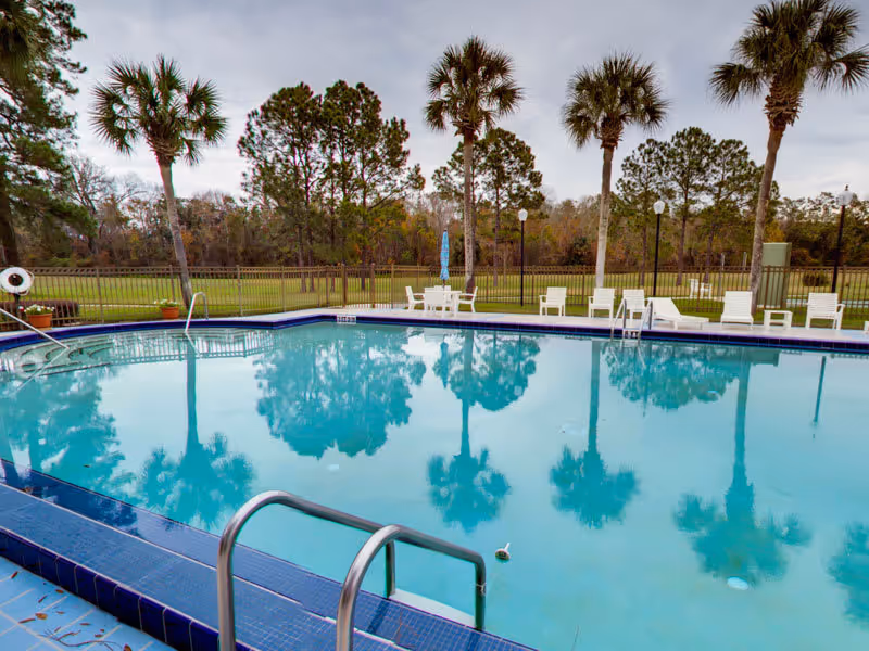 Outdoor swimming pool with lounge chairs and palm trees reflected in the water.