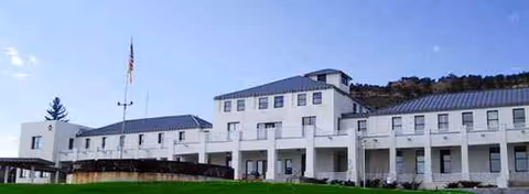 White multi-story senior care facility exterior with a flagpole and manicured lawn.