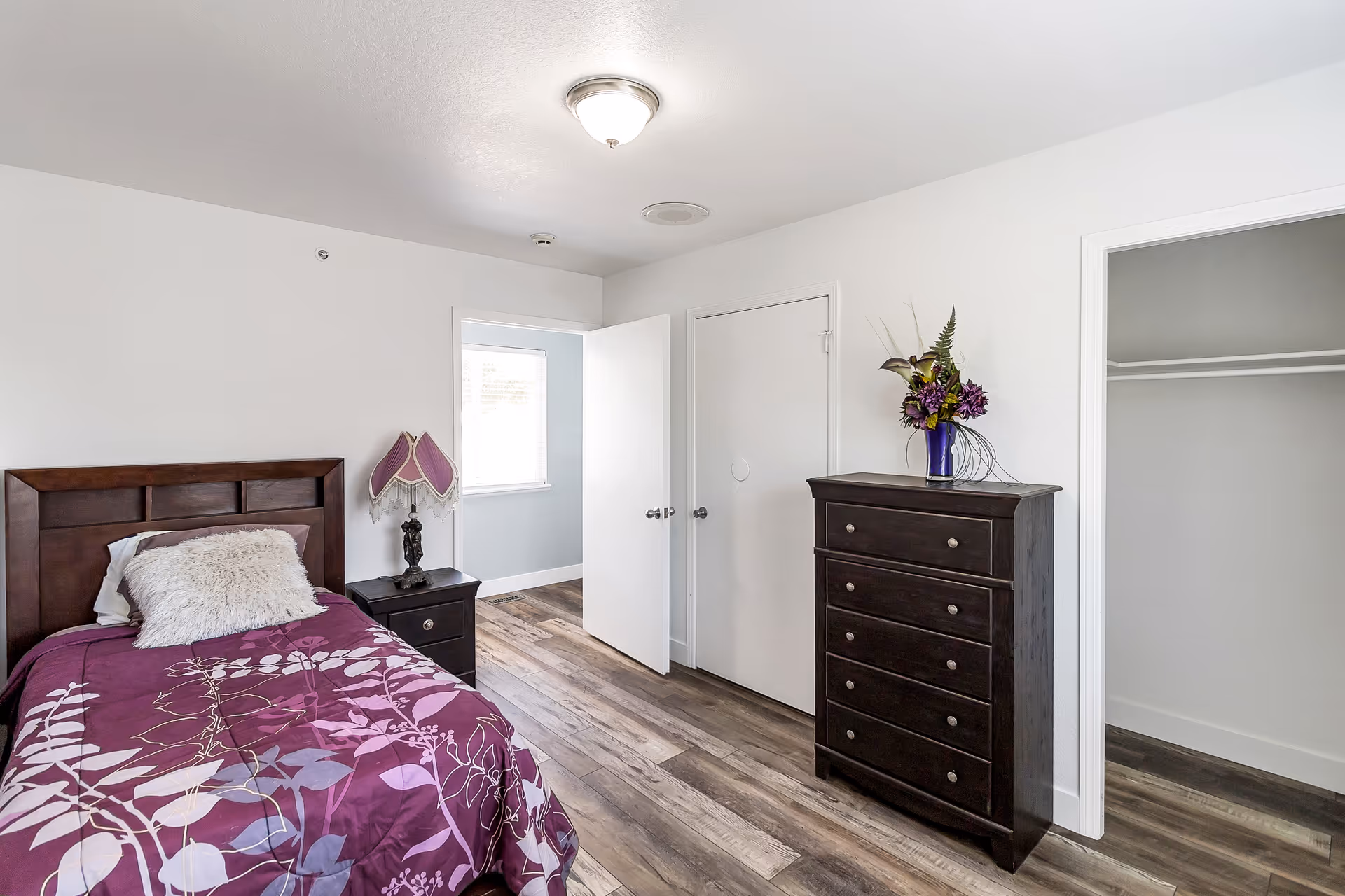 Bedroom with a single bed, dark wood dresser, nightstand, and open closet.