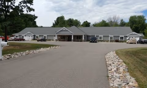 Single-story senior living facility with a long front entrance, paved driveway, and parked cars.