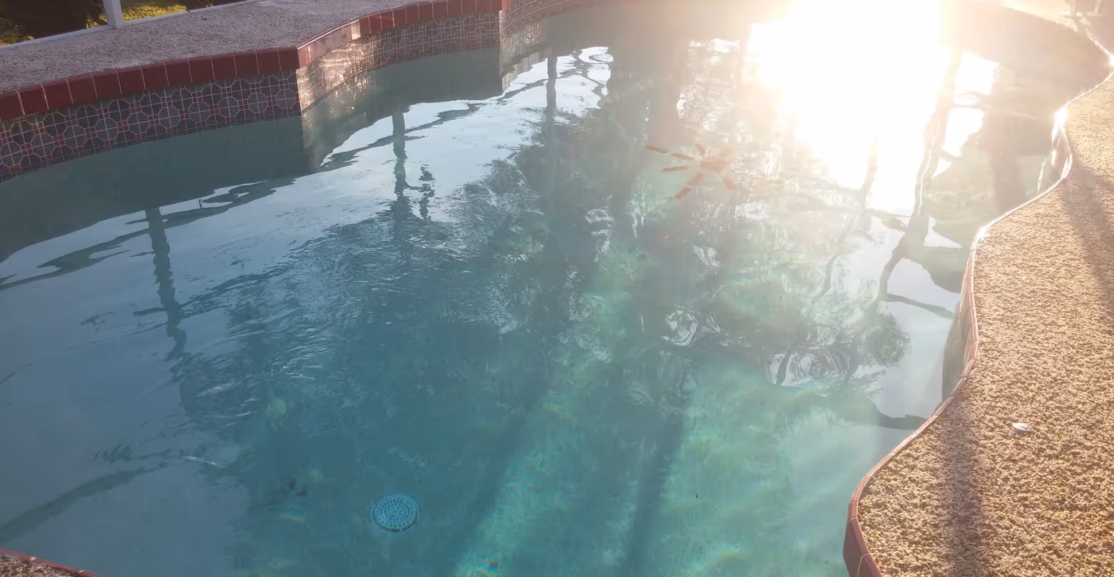Outdoor pool with blue water, sunlight glare, and tiled edge reflecting shadows.