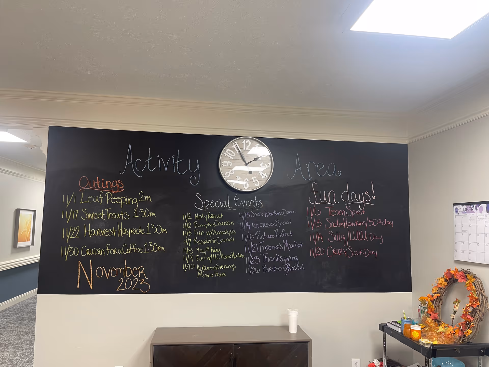 Chalkboard activity board with a clock above listing November events in a senior living facility common area