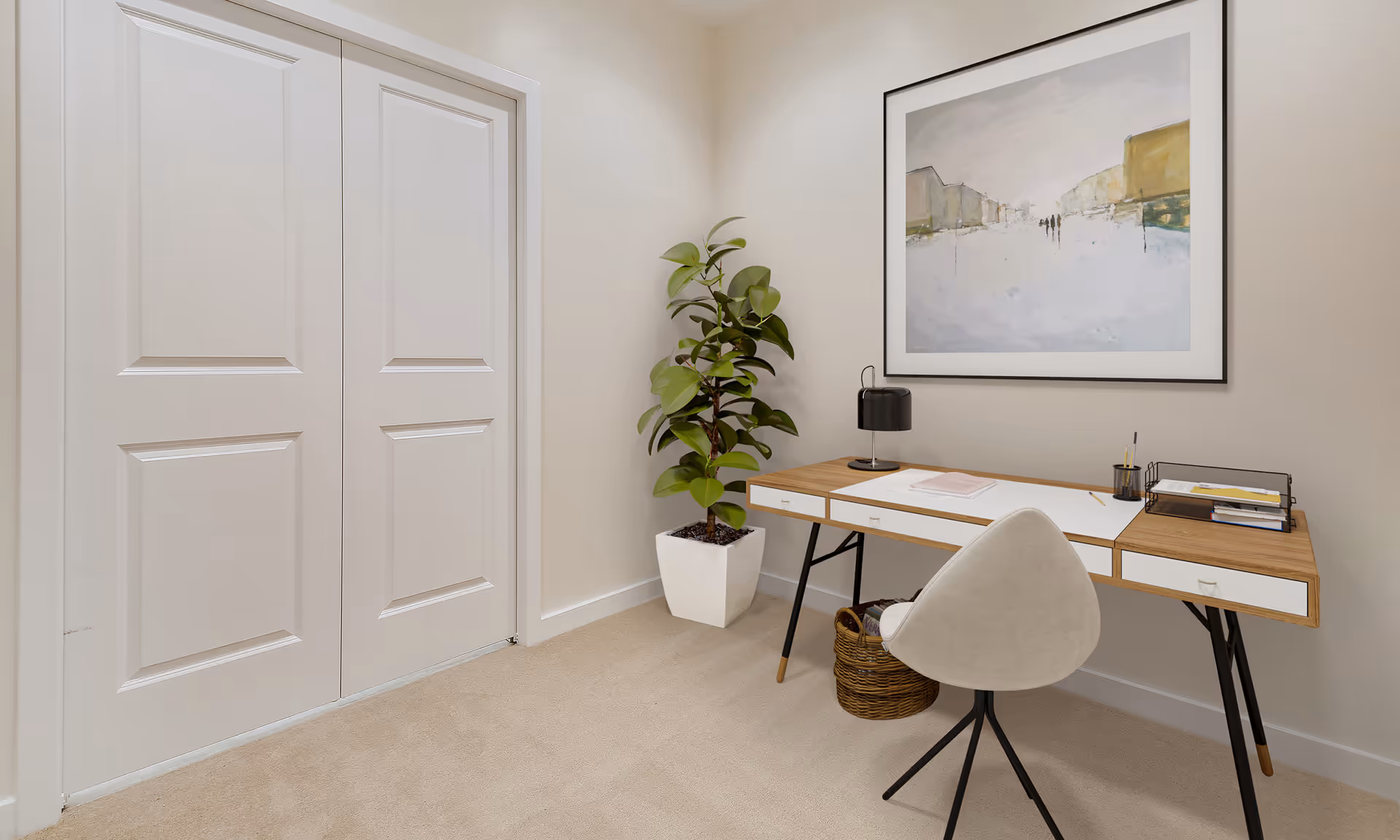 Small home office nook with a desk, chair, potted plant, wall art, and closed double closet doors.