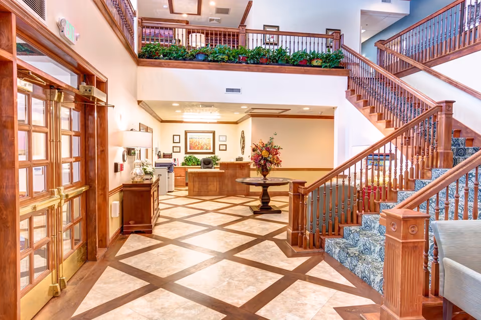 Bright lobby with a wooden staircase, reception desk, and patterned tile floor.