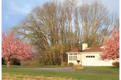 White retirement residence with a driveway, pink flowering trees, and bare trees in the background.