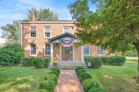 Two-story brick senior living building with front steps, bunting, and trimmed landscaping.