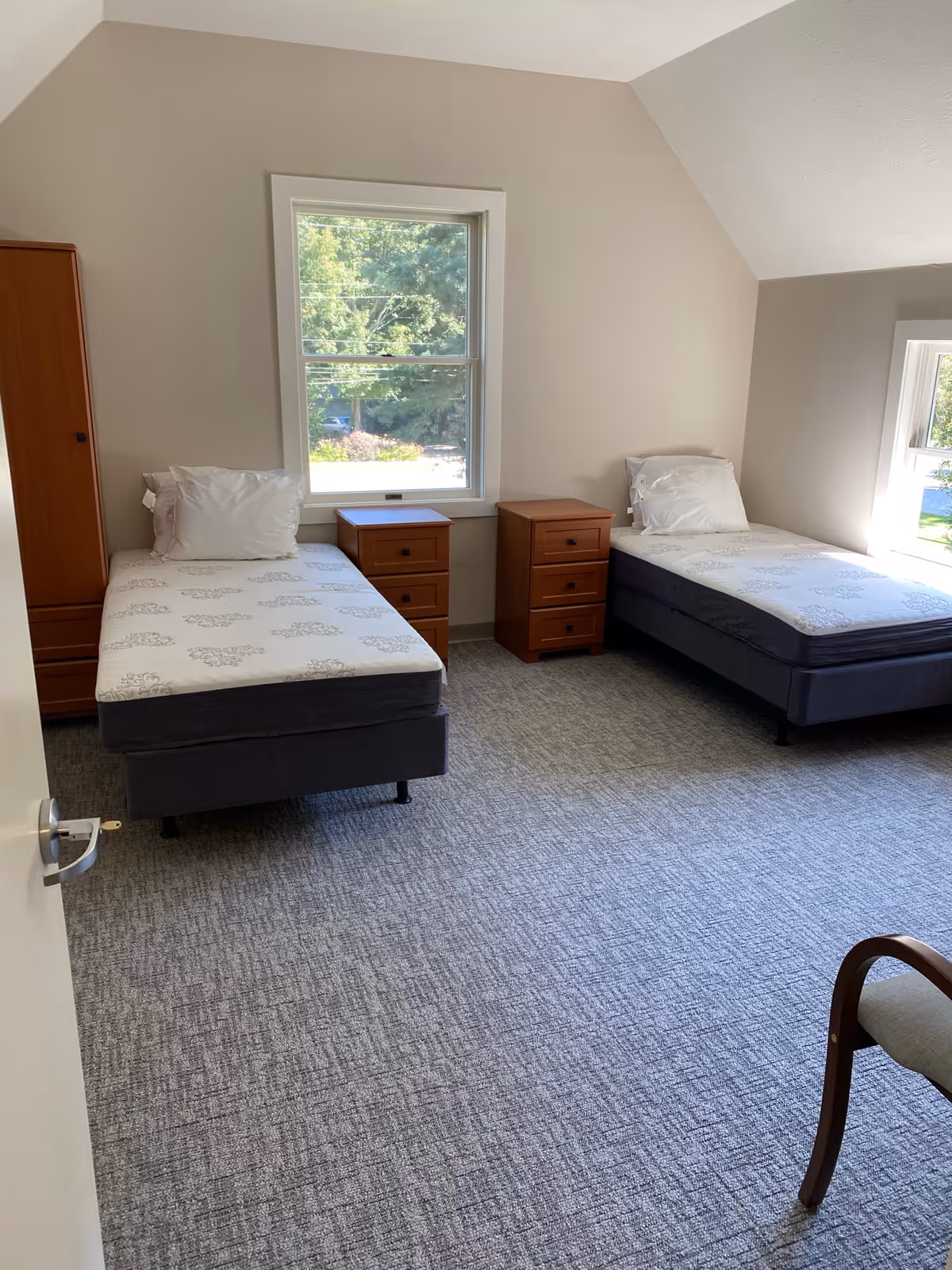 Bright bedroom with two single beds, matching wooden nightstands and a window overlooking greenery.