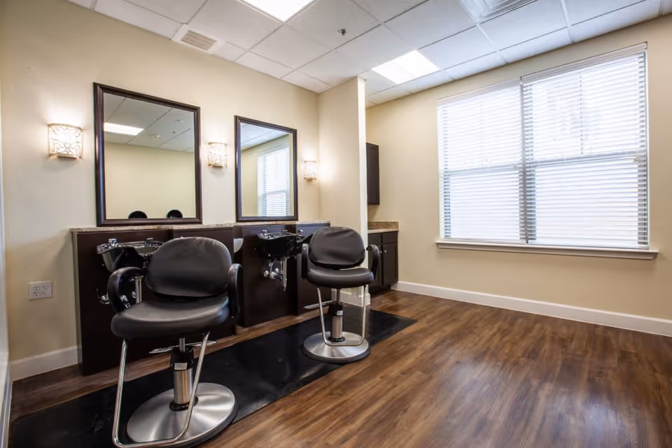 Interior salon with two styling chairs and wash sinks in front of mirrors beside a large window.