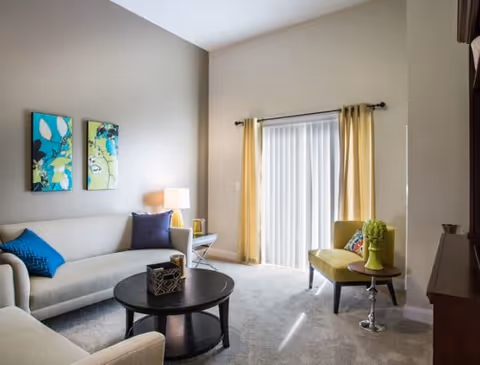 Bright living room with a sofa, armchair, round coffee table, and sliding glass door with yellow curtains.