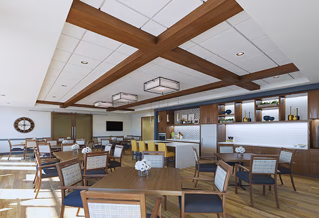 A bright, open dining room with multiple wooden tables and chairs, a central kitchen/bar area, and decorative wooden ceiling beams.