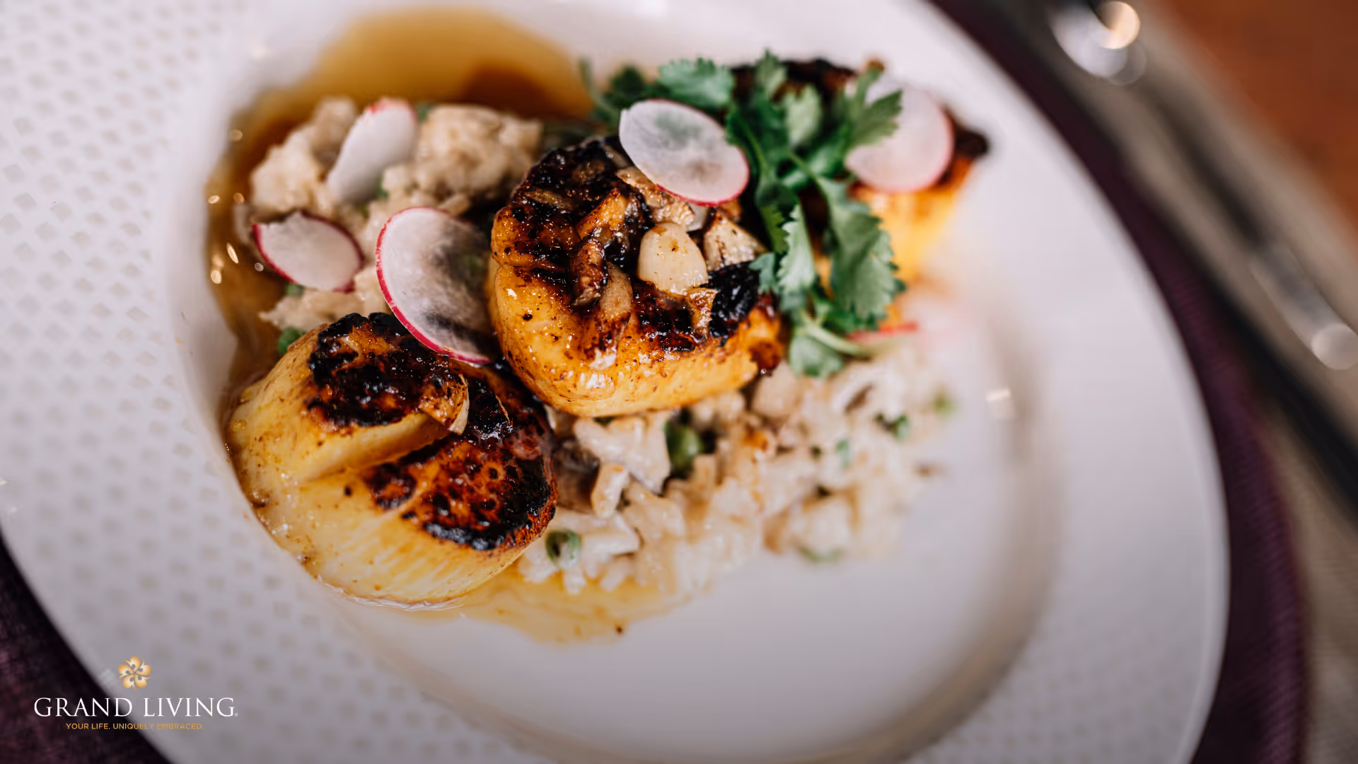 Close-up of seared scallops on a bed of risotto garnished with radish slices and herbs on a white plate.