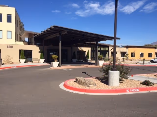 Exterior view of The Watermark at Cherry Hills building entrance with a covered drop-off area, large planters, and a roundabout driveway under a clear blue sky.