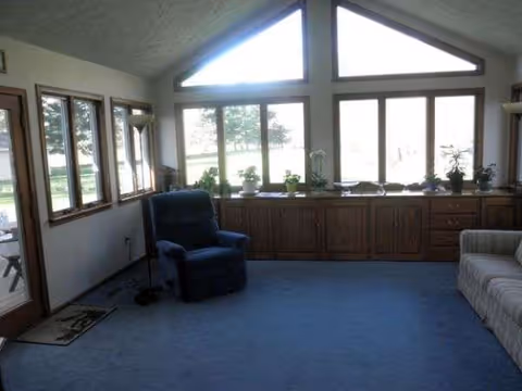 A bright living room in a senior facility with a blue recliner and large windows.