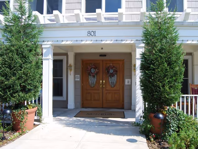 Double wooden entrance doors with wreaths under a covered porch numbered 801, flanked by potted evergreen shrubs.