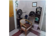 Small corner salon area with two hooded hair dryers, a chair, shelving with supplies, and a waste bin.