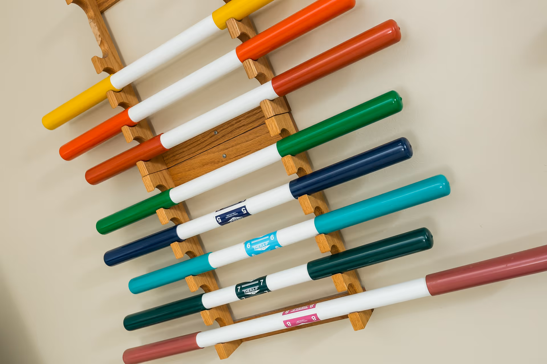 Wooden wall rack holding multiple colorful exercise or therapy bars.