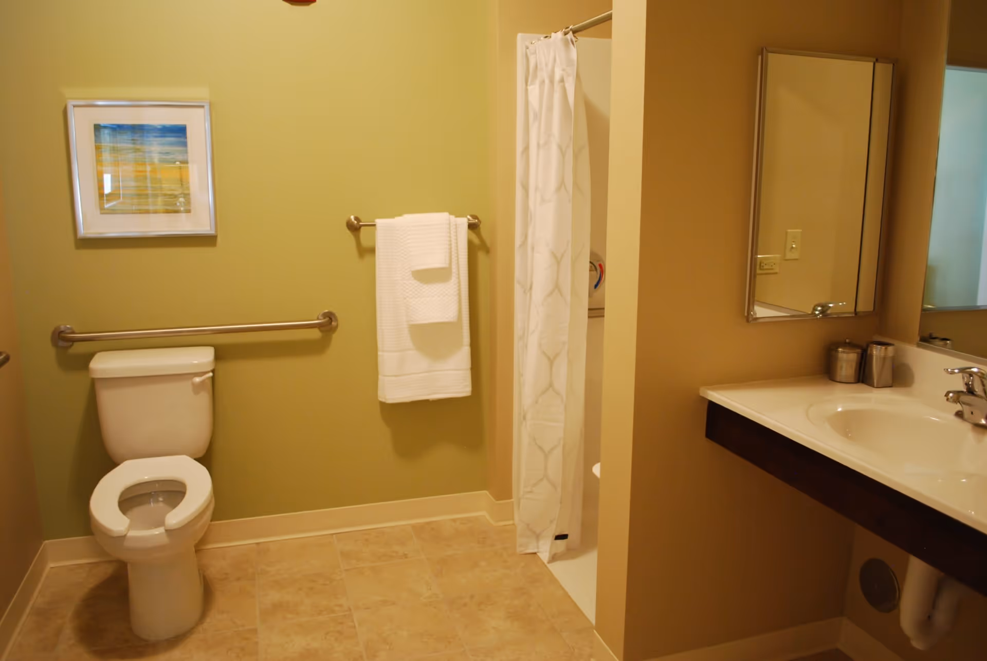 A clean bathroom with a toilet, a towel hanging on a rack, a shower with a white curtain, a sink with a mirror above it, and a framed picture on the wall.