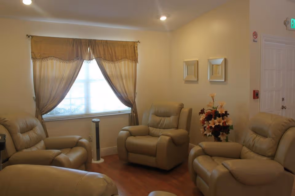 Cozy sitting room with beige leather recliners, a curtained window, and a floral arrangement.