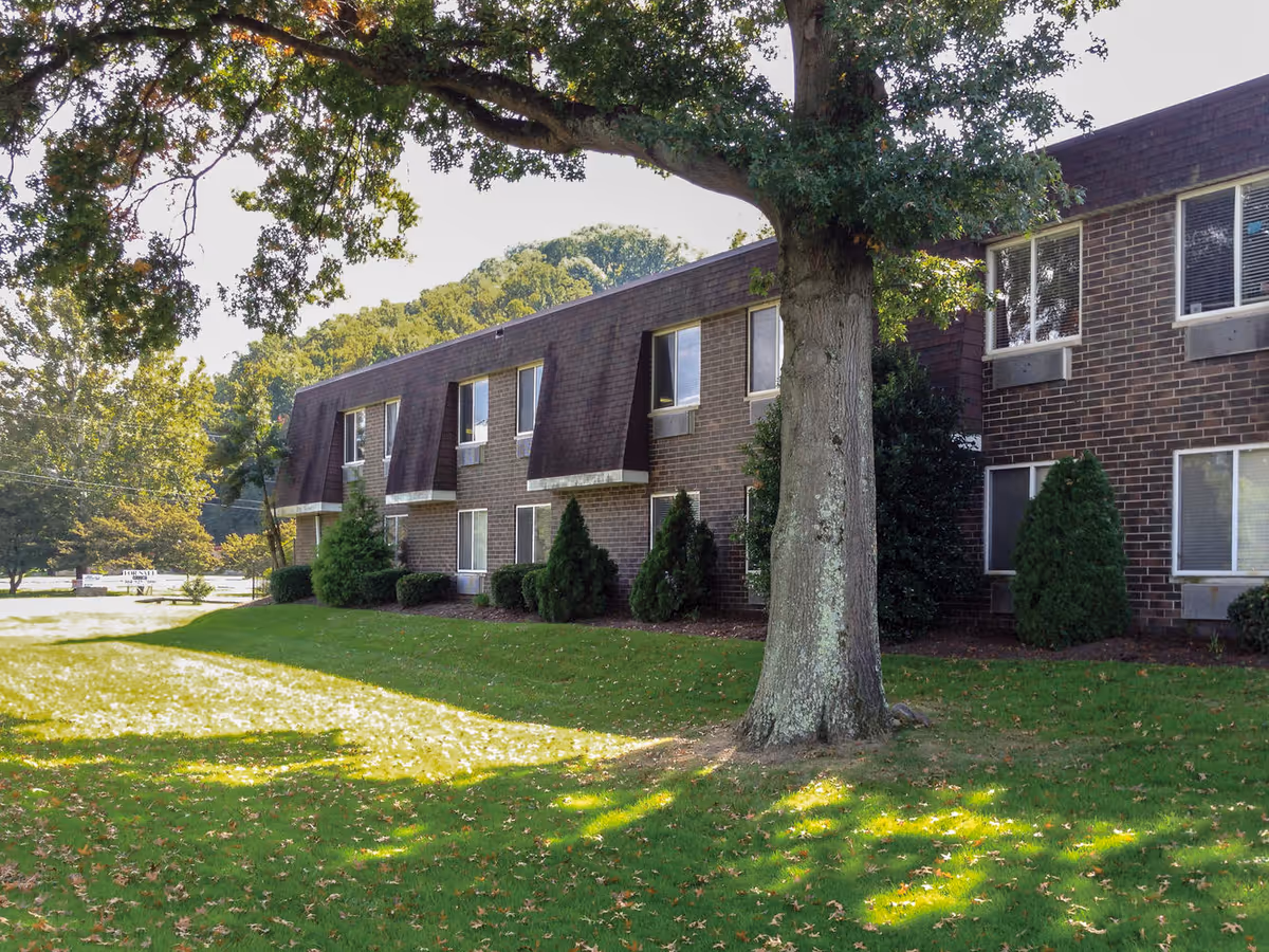 Two-story brick healthcare building with a large tree and grassy lawn in front.
