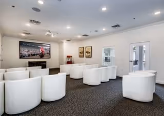 Carpeted media room with rows of white barrel chairs facing a large wall-mounted TV and a popcorn machine.