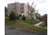 Exterior view of a brick senior living facility on a grassy hill with a walkway.