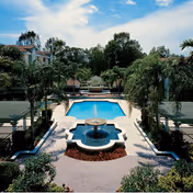 Landscaped outdoor courtyard with a central pool and fountain flanked by palm trees and residential buildings.