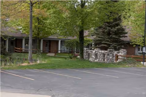 Exterior view of Yorkshire Manor with trees, stone feature, and benches by parking.