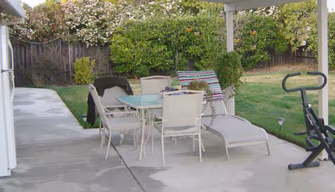 Outdoor patio with table, chairs, lounge chairs, and exercise equipment in a courtyard.