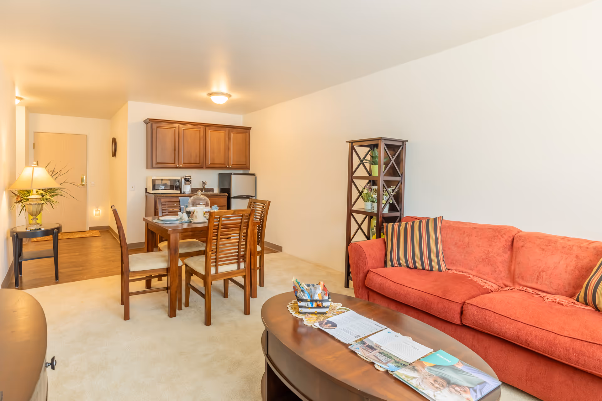 Open living and dining area featuring a red sofa, wooden coffee table, dining set and a small kitchenette.